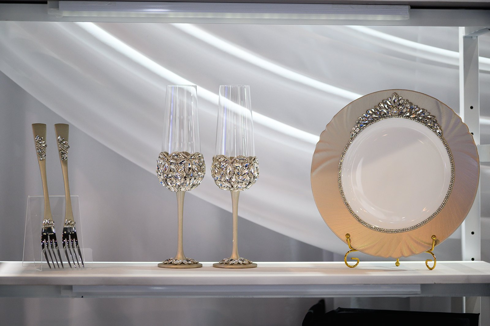 Glory Classic luxury wedding set display featuring champagne gold crystal-embellished flutes, handpainted plate with floral crystal border, and matching forks with black crystal handles on elegant shelf