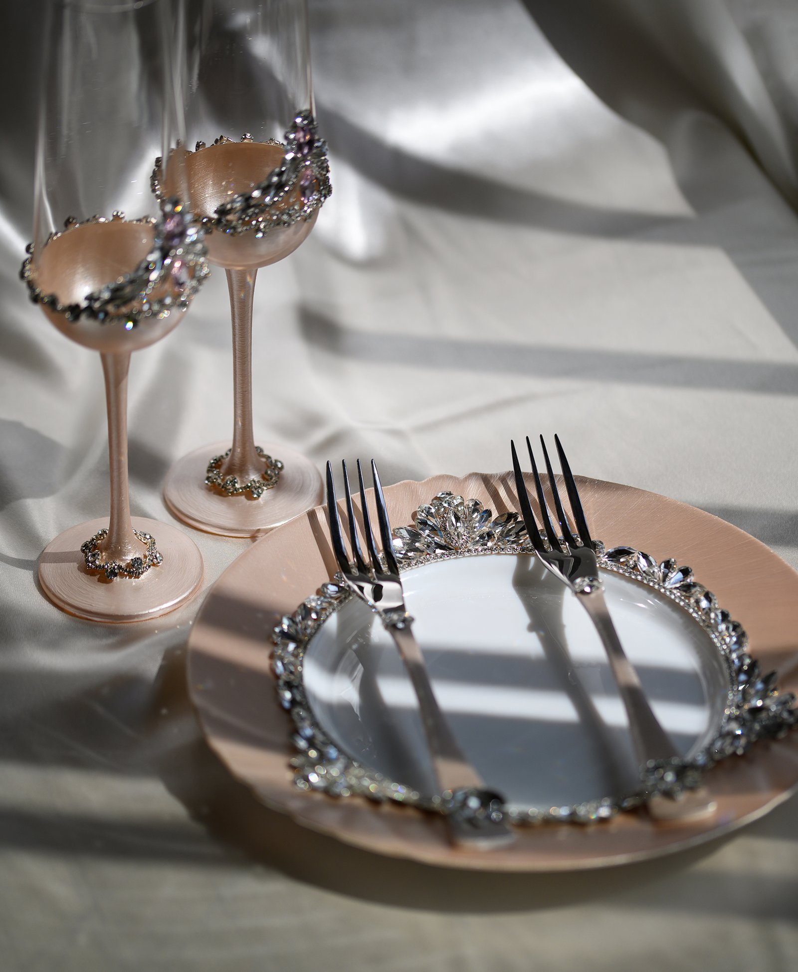 Grace Classic luxury wedding set featuring rose gold champagne flutes with pink crystal crown rim, crystal-embellished plate with floral accents, and elegant black crystal forks in natural light