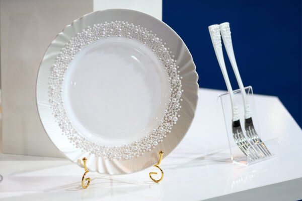 Pearl Classic handpainted white plate with densely arranged pearl border and scalloped edge, displayed on gold stand with matching white pearl-adorned forks against navy blue background