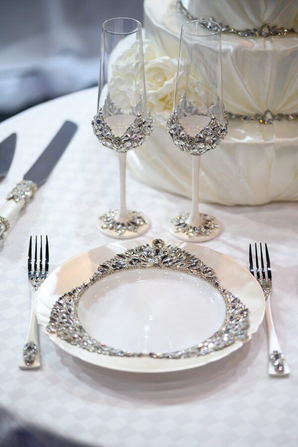 Crystal-embellished champagne flutes and matching dinnerware from Ethereal collection with white wedding cake