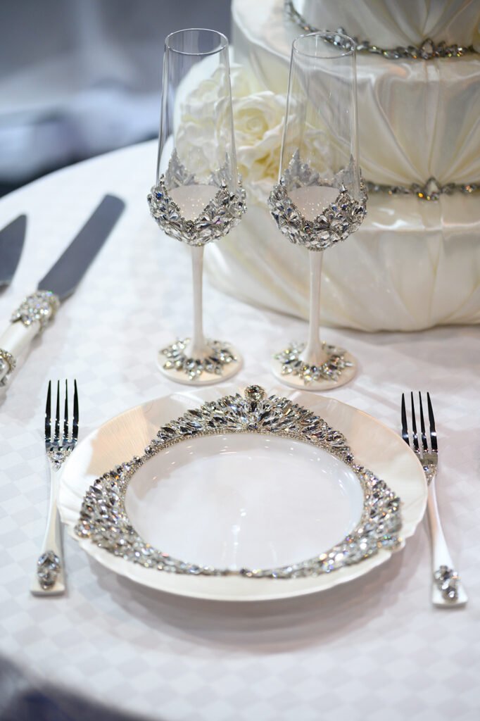 Crystal-embellished champagne flutes and matching dinnerware from Ethereal collection with white wedding cake